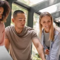 Grupo diverso de pessoas colaborando em um projeto em ambiente moderno, focando na inovação e criatividade. Todos observam um laptop em mesa.